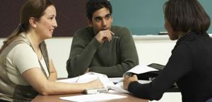 Woman sitting on a sofa teaching a young girl how to crochet